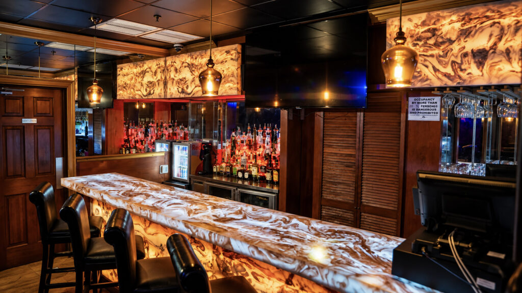 The upstairs VIP bar with a backlit onyx bar top and amber pendant lights at Rachel's North in Casselberry, Florida